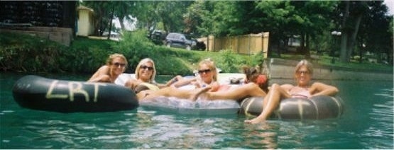 Isabelle the Silky Terrier is standing on a tube that is between Four Women who are also floating on tubes