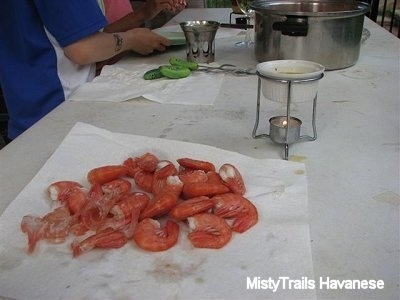 The backside of Prawns on a paper towel. There is a cup of butter and next to that is a pot of other Prawns.