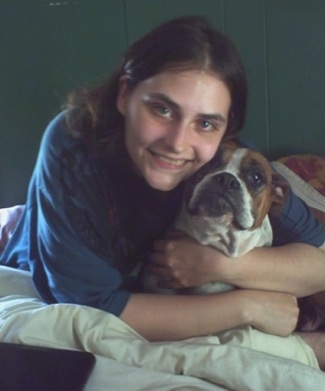 Baby Girl the Boxer being hugged by its owner in a bed