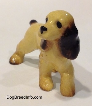 A tan with black and brown Cocker Spaniel ceramic figurine is looking to the left.