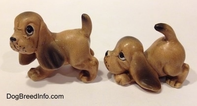 The left side of two Vintage miniature ceramic Bloodhound figurines. The ears of the figurines are easily visible against the body.