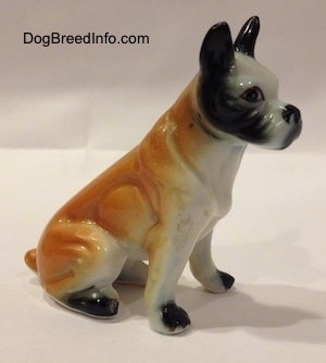 The right side of a red and white with black bone china Boxer figurine that is in a sitting pose. The figurine has black paws.