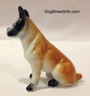 The left side of a red and white with black bone china Boxer figurine that is in a sitting pose. The figurine has great arm details.