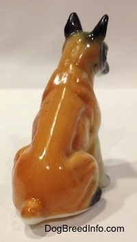 The back right side of a red and white with black bone china Boxer figurine that is in a sitting pose. The figurine is glossy.