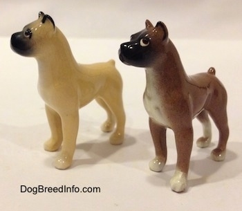 The front left side of two color variations of a miniature Boxer dog standing figurine. Both figurines have short tails.