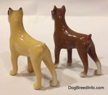 The back left side of two color variations of a miniature Boxer dog standing figurine. The figurines are glossy.