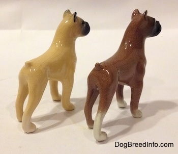 The back right side of two color variations of a miniature Boxer dog standing figurine. The ear tips of both figurines are black.