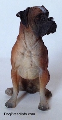 A brown with black and white Boxer Boxer figurine in a sitting pose and it is made out of resin. The figurine has great details on its face.