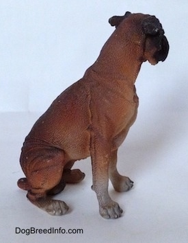 The right side of a brown with black and white Boxer figurine that is in a sitting pose and it is made out of resin. The figurine has white paws.