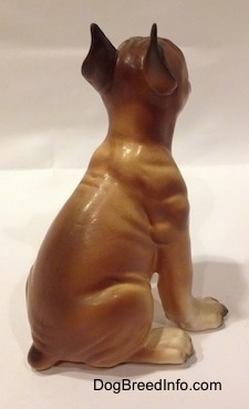 The back right side of a brown with black and white Boxer puppy figurine. The figurine has detailed muscle definition.