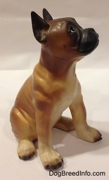 The front left side of a brown with black and white Boxer puppy figurine. The figurine has a black muzzle.
