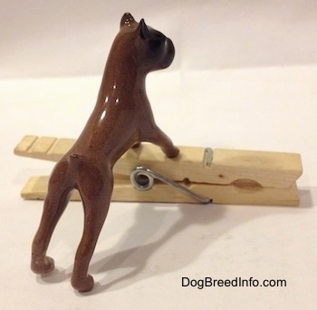The back right side of a brown with black Boxer dog figurine that is placed on top of a clothespin. The figurine lacks fine details.