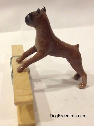 The left side of a brown with black Boxer dog figurine that is placed on top of a clothespin. The figurine has a short tail.