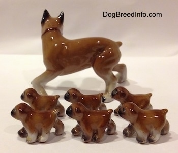 The left side of a brown with white and black Boxer mom with 6 puppies figurines. All of the figurines have short tails.
