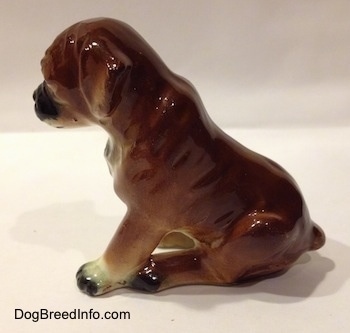 The left side of a brown with black and white ceramic Boxer puppy figurine with uncropped ears in a sitting pose. The paws of the figurine are connected.