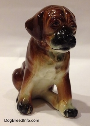 A brown with black and white ceramic Boxer puppy figurine with uncropped ears in a sitting pose. The figurine is very detailed.