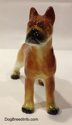 A brown with black and white ceramic Boxer dog figurine. The figurine has little black circles for eyes.
