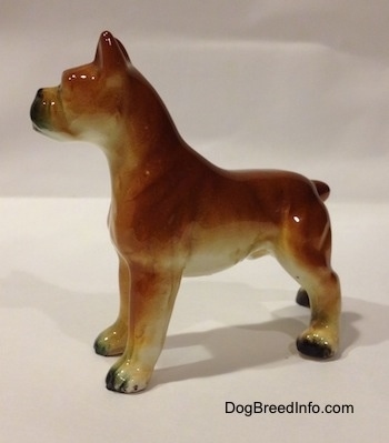 The left side of a brown with black and white ceramic Boxer dog figurine. The figurine has a detailed body and legs.