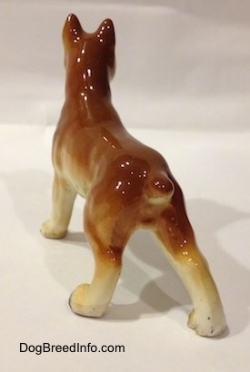The back of a brown with black and white ceramic Boxer dog figurine. The figurine has a small detailed tall.