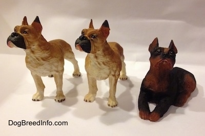 Two tan with white and black Boxer figurines are placed next to a black with brown laying Boxer figurine.
