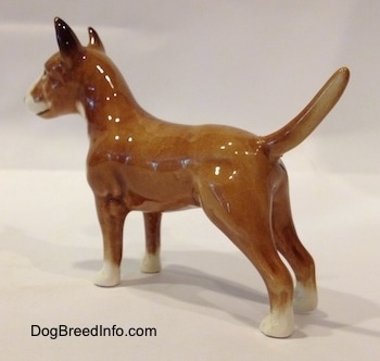 The back left side of a brown with white Bull Terrier figurine. The figurines tail is long.