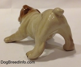 The back left side of a tan with brown Bulldog puppy figurine that is in a play bow pose. The figurine has fine details on its body.