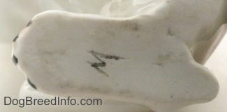 Close up - The underside of a white with brown Bulldog figurine. On the underside there is a M or W mark on the paw.