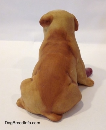 The back of a tan with white Bulldog puppy figurine that has a red slipper shoe under it. The figurine has a medium sized tail.