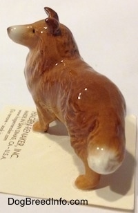 The back left side of a figurine that is a brown with white Collie dog. The figurine has white a tipped tail.