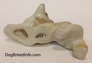 The underside of a tan and white bone china Coyote figurine that is in a play bow pose. There is a faded JAPAN stamp on the underside.