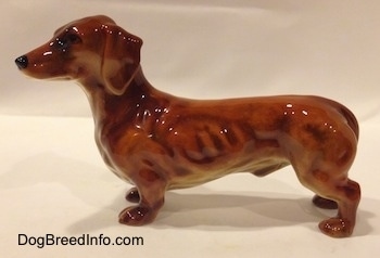 The left side of a figurine of a brown Dachshund. The figurine has long ears and it is attached to its body.