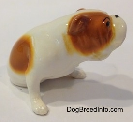 The front right side of a white with red Bulldog figurine that is in a sitting pose. The figurine has a black dot for a nose.