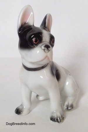The front left side of a white and black French Bulldog in a sitting pose figurine. The figurine has white paws and black nails.