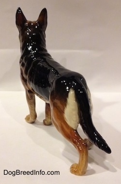The back left side of a black and tan figurine of a German Shepherd standing. The figurine has a tail going down one of the hind legs.