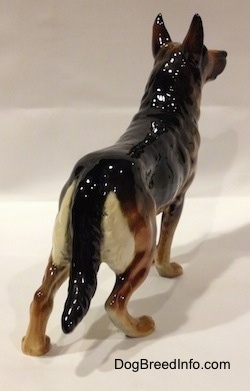 The back right side of a figurine of a black and tan German Shepherd standing. The figurines ears are in the air.