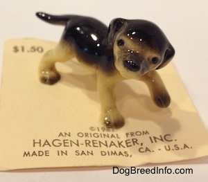 The front right side of a black with tan figurine of a standing German Shepherd puppy. The figurines ears are flopped over and hard to differentiate from its head.