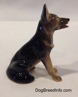 The right side of a black with tan figurine of a German Shepherd sitting. The figurine has its ears in the air.