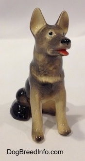 A black with grey and tan German Shepherd sitting figurine that has its mouth open.