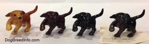 Four Labrador Retriever puppys in different color variation figurines with there paws in the air. The figurines are glossy.