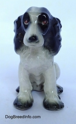 A black with white Russian Spaniel dog figurine in a sitting pose. The figurine has red eyes.