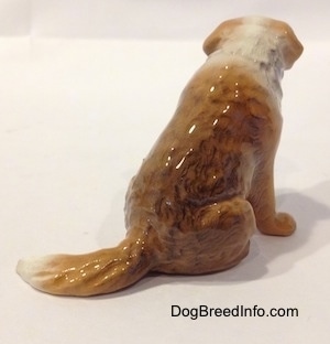 The back right side of a brown with white figurine of a Saint Bernard sitting. The figurines has a long tail.