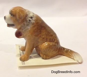 The left side of a brown with white figurine of a Saint Bernard sitting. The figurines mouth is painted to look like ts tongue is sticking out.