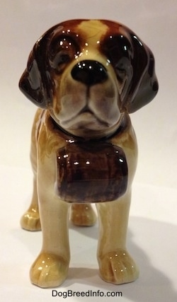 A white with dark tan porcelain Saint Bernard dog figurine. The figurine is wearing a barrel collar.