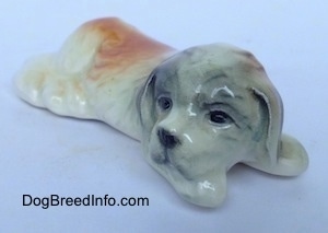 The front right side of a Saint Bernard puppy in a lying position figurine. The ears of the figurine are tinted black.