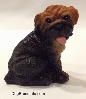 The right side of a black with brown Shar-Pei puppy that is made out of resin. The tail of the figurine is hanging out of its mouth.