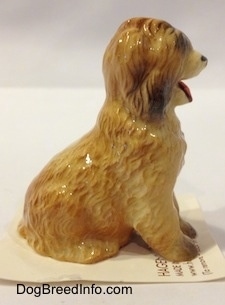 The right side of a tan with brown Sheepdog that is in a sitting pose figurine. The figurine has long legs.