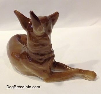 The front right side of a brown with white Shepherd lying figurine. The figurine has fine hair details.