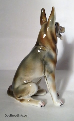 The right side of a brown and white with black German Shepherd sitting figurine. The figurine has long legs.