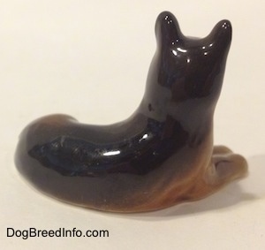 The back right side of a brown with black Shepherd in a lying pose figurine. The figurine is glossy.