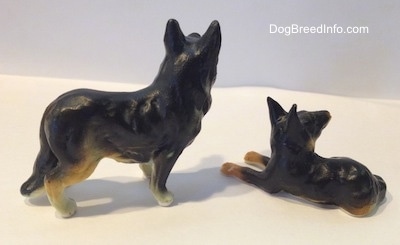 The right side of a porcelain black with tan German Shepherd standing figurine that is next to a laying black with tan German Shepherd figurine.